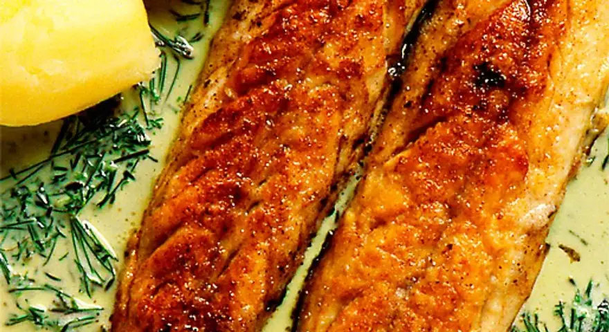 Två gyllene filéer av stekt makrill i en krämig sås med dill och kokt potatis.