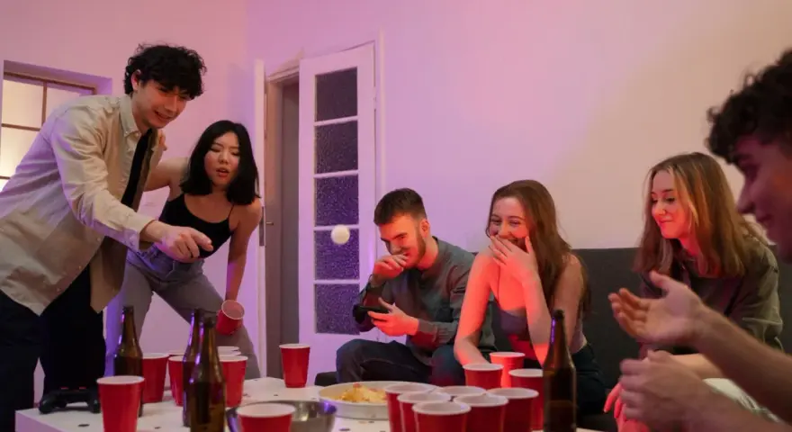 Unga vänner spelar beer pong, en rolig aktivitet med röda muggar och skratt.
