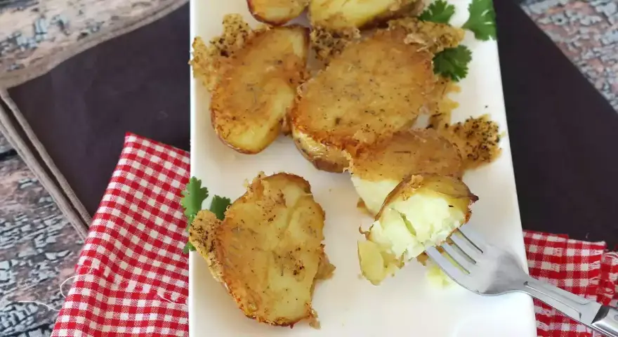 Krispiga, gyllene smashed potatis på en vit tallrik, garnerade med persilja. En gaffel visar en mjuk insida.