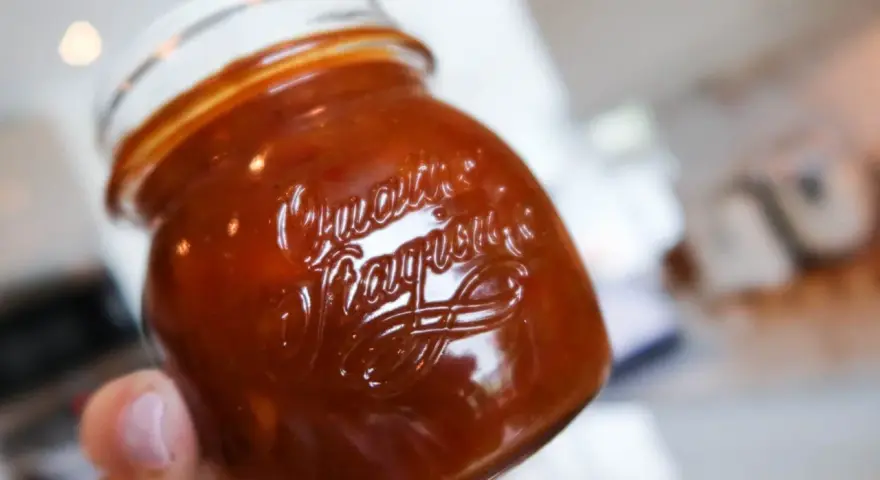 En hand håller ett glas med en mörkröd rabarber chutney.