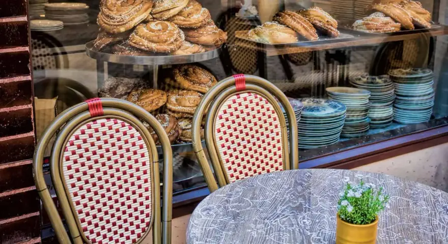 Två stolar med flätad sits och ryggstöd framför ett skyltfönster med kanelbullar och andra bakverk. Ett annorlunda café med charmig inredning.