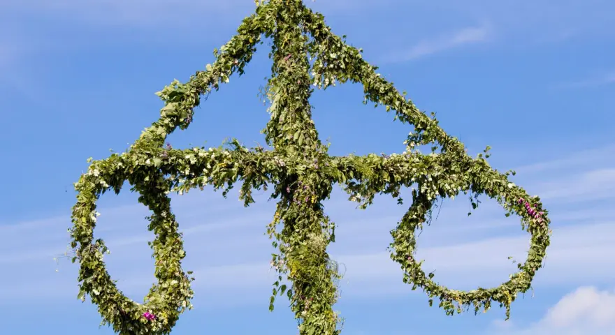 En midsommarstång, dekorerad med grönska och blommor, mot en blå himmel. En symbol för sommar och glädje, en viktig del av fakta om midsommar.