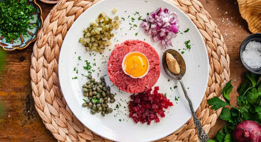 En tallrik med råbiff, äggula, kapris, rödlök, hackad gurka och rödbetor. Perfekt för ett klassiskt råbiff recept.