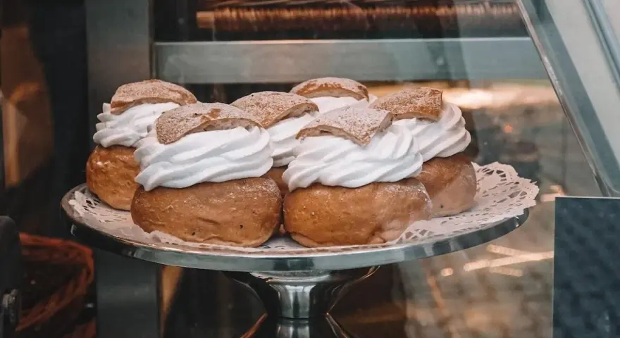 Sju semlor på ett fat, redo för pannkakans dag. Krämig grädde och pudrat socker.