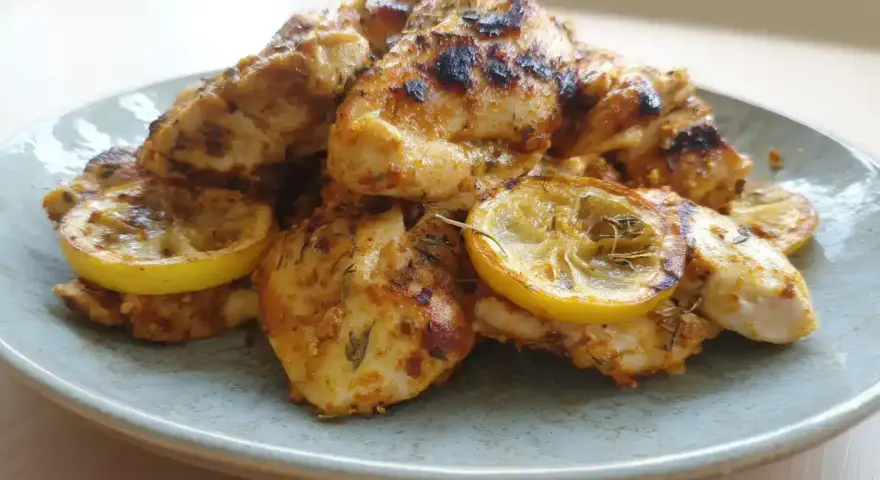 Grillad, saftig marinad kyckling med citronskivor på en ljusblå tallrik. Perfekt för en sommarfest!