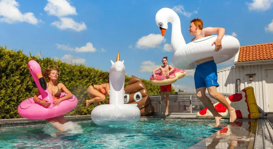 Ungdomar hoppar i poolen med uppblåsbara badleksaker som flamingo, enhörning och bajskorv. Perfekt för midsommarlekar inomhus eller utomhus!