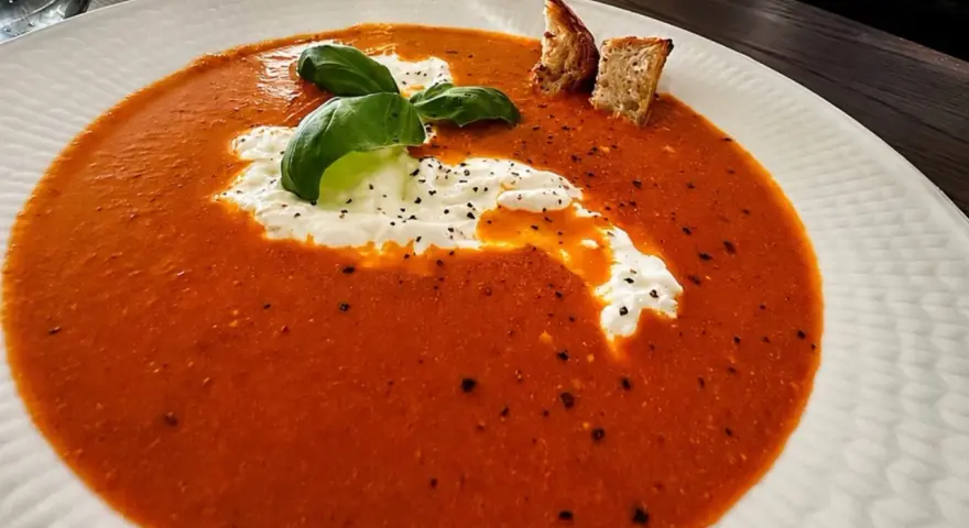 En krämig tomatsoppa med en klick gräddfil, färsk basilika och krutonger. Perfekt som en del av ett tomatsoppa recept.