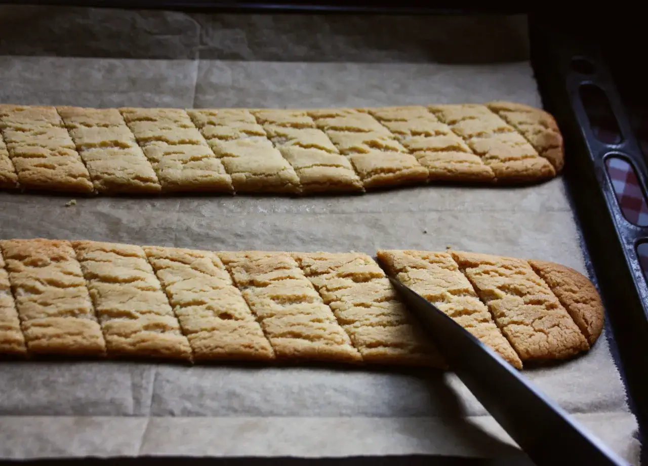 Två långa, gyllene sirapssnittar på bakplåtspapper, en kniv skär i den nedre kakan. Perfekt för sirapssnittar recept.