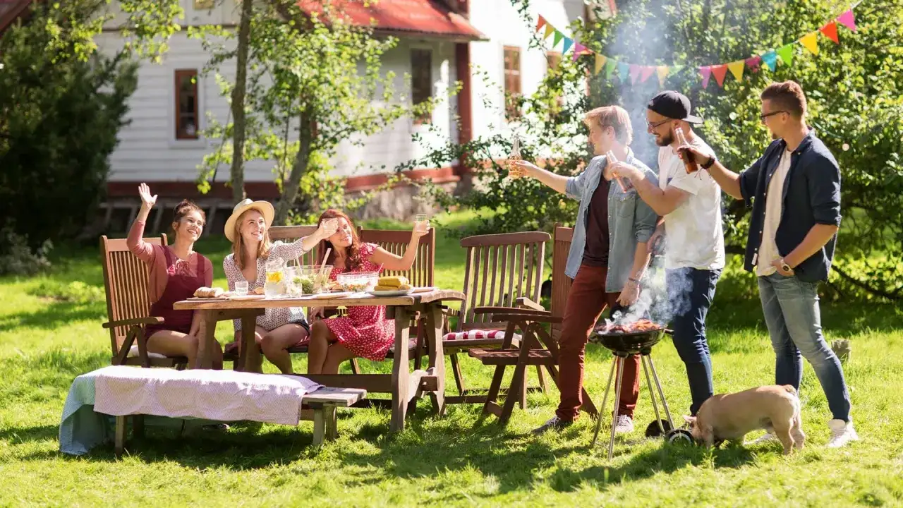 V&auml;nner njuter av grillfest och lekar i tr&auml;dg&aring;rden. En hund nosar i gr&auml;set.