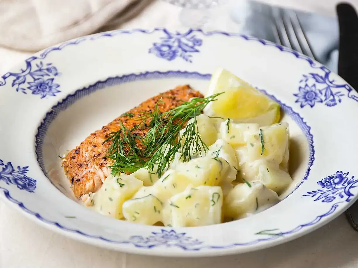 En saftig laxfilé med en klyfta citron och en generös portion krämig dillstuvad potatis.