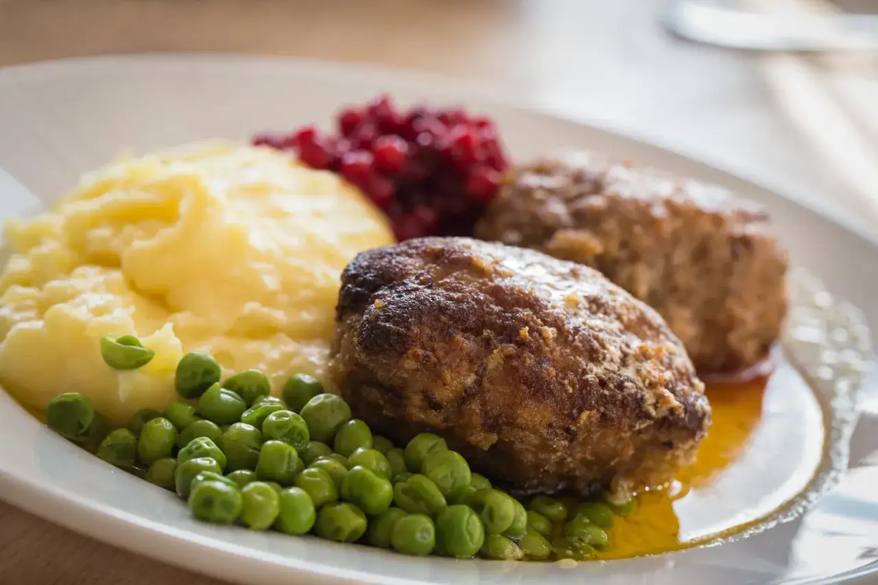 En tallrik med Wallenbergare, potatismos, gröna ärtor och rårörda lingon. Ett klassiskt svenskt recept.