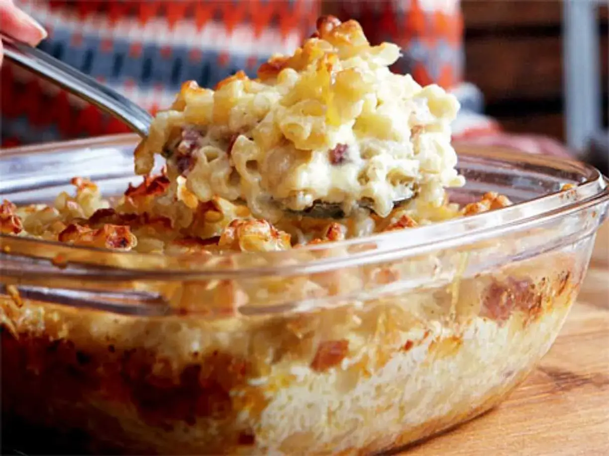 En sked lyfter upp en portion krämig, gammaldags makaronipudding ur en glasform.