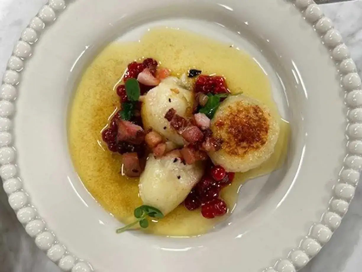 Kroppkakor recept: Potatisdumplings med lingon, bacon och en gyllene s&aring;s p&aring; en vit tallrik.