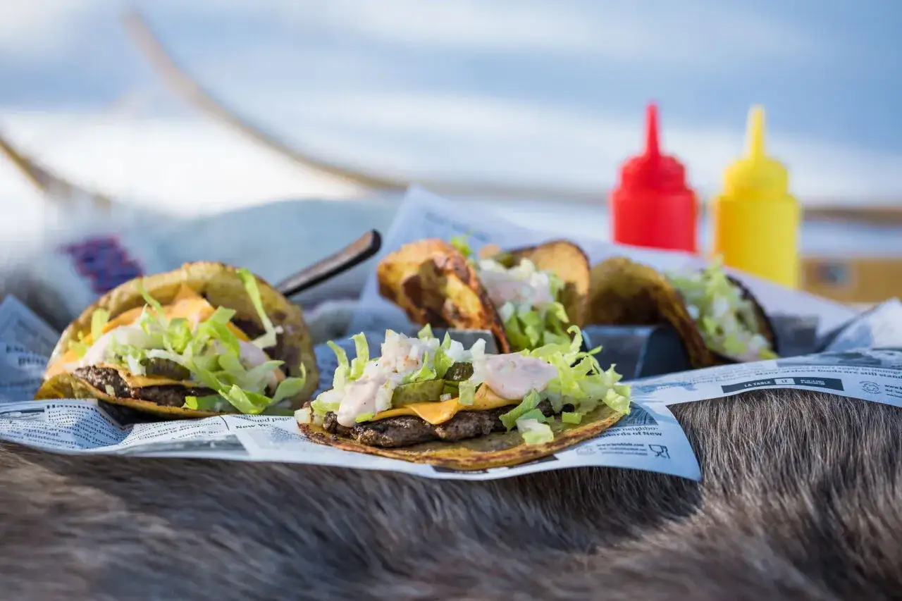 Lyxig mat utomhus: tacos med kött, ost och sallad, serverade på tidningspapper med ketchup och senap i bakgrunden.