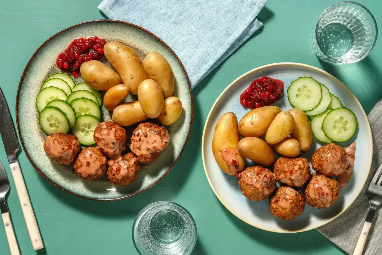 Två tallrikar med köttbullar, småpotatis, gurka och lingonsylt. Ett perfekt recept middag för två.