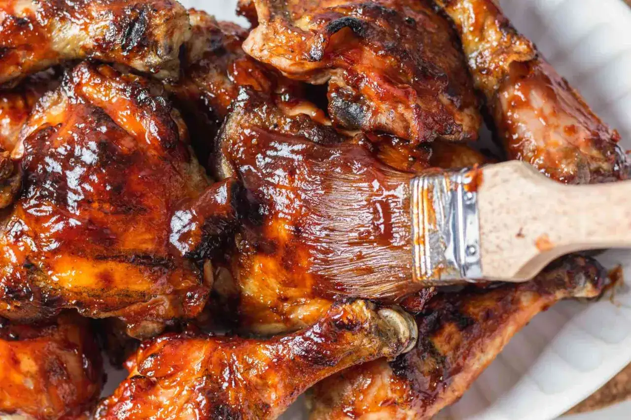 En pensel applicerar glaze på saftig, grillad kyckling. Perfekt för en sommarkväll med grillning av kyckling.