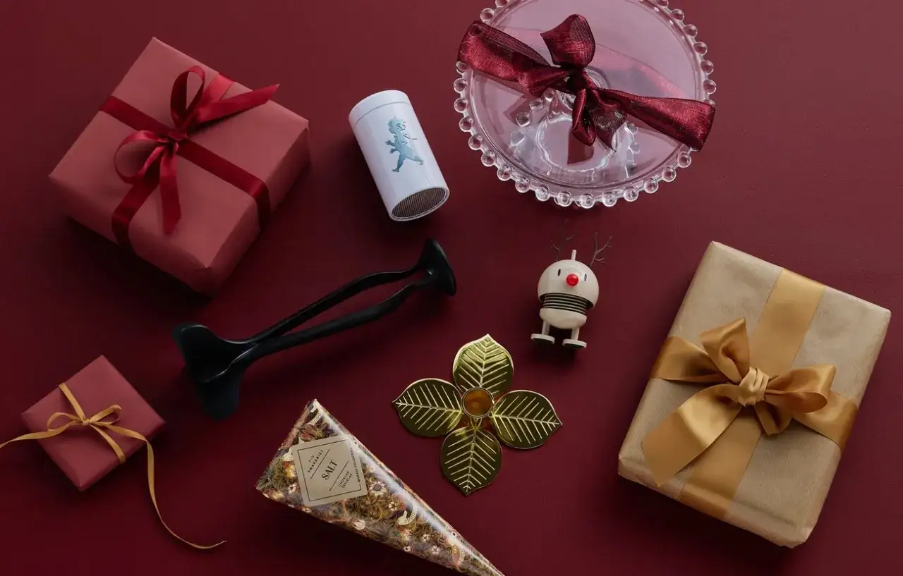 Julklappsspelet regler: alla f&aring;r en julklapp. Presenter i r&ouml;tt och guld, en liten tomte och en glasbricka.