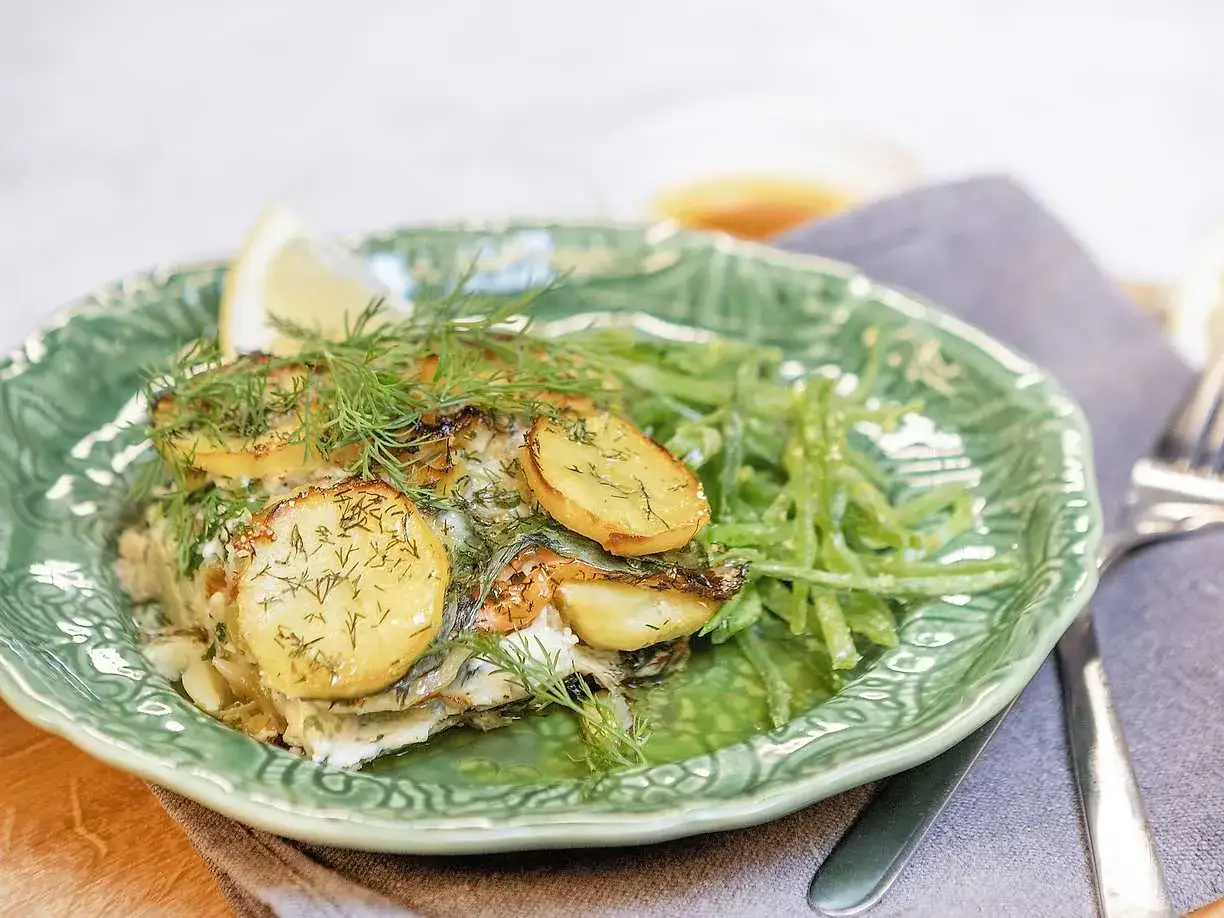 Laxpudding recept: en l&auml;cker r&auml;tt med lax, potatis och dill p&aring; en gr&ouml;n tallrik, serverad med gr&ouml;na b&ouml;nor.