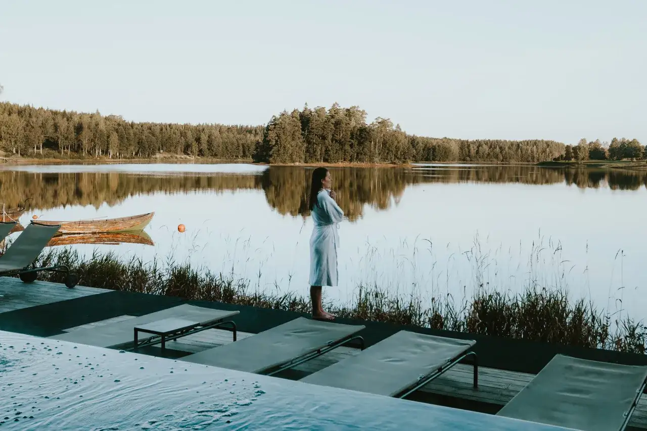 En kvinna i morgonrock njuter av lugnet vid en sj&ouml;, en idyllisk upplevelse av spa i Sverige.