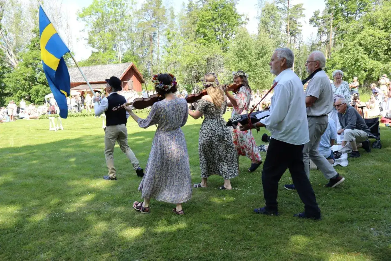 En grupp spelar fiol och en person b&auml;r en svensk flagga. En fin scen som ger fakta om midsommar.