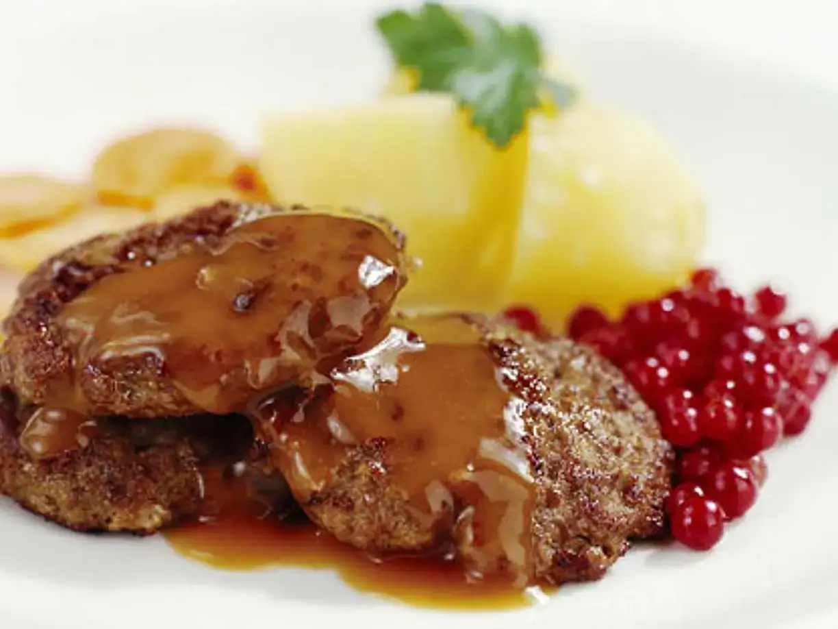 Två köttbullar med en härlig brun sås, serverade med potatis och lingon. En klassisk svensk rätt som smakar underbart.