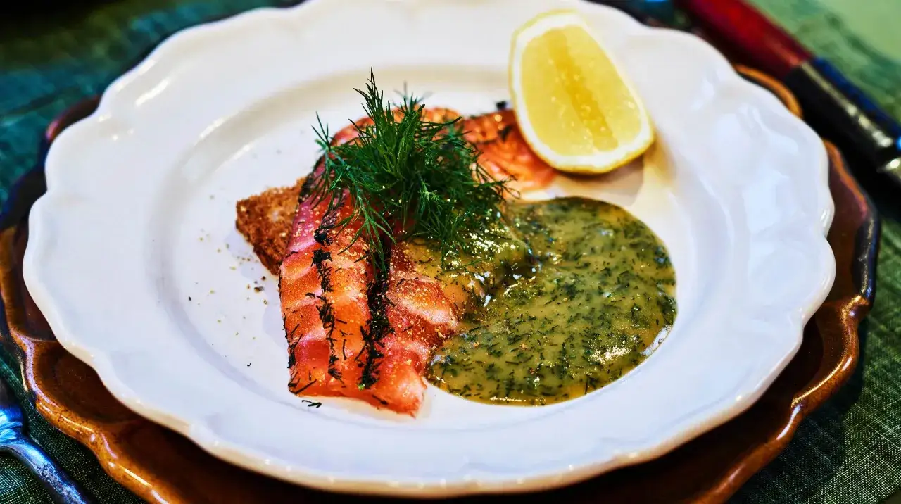 En vacker tallrik med gravad lax, dill och en krämig sås till laxen. Serveras med en citronklyfta och en bit rågbröd.
