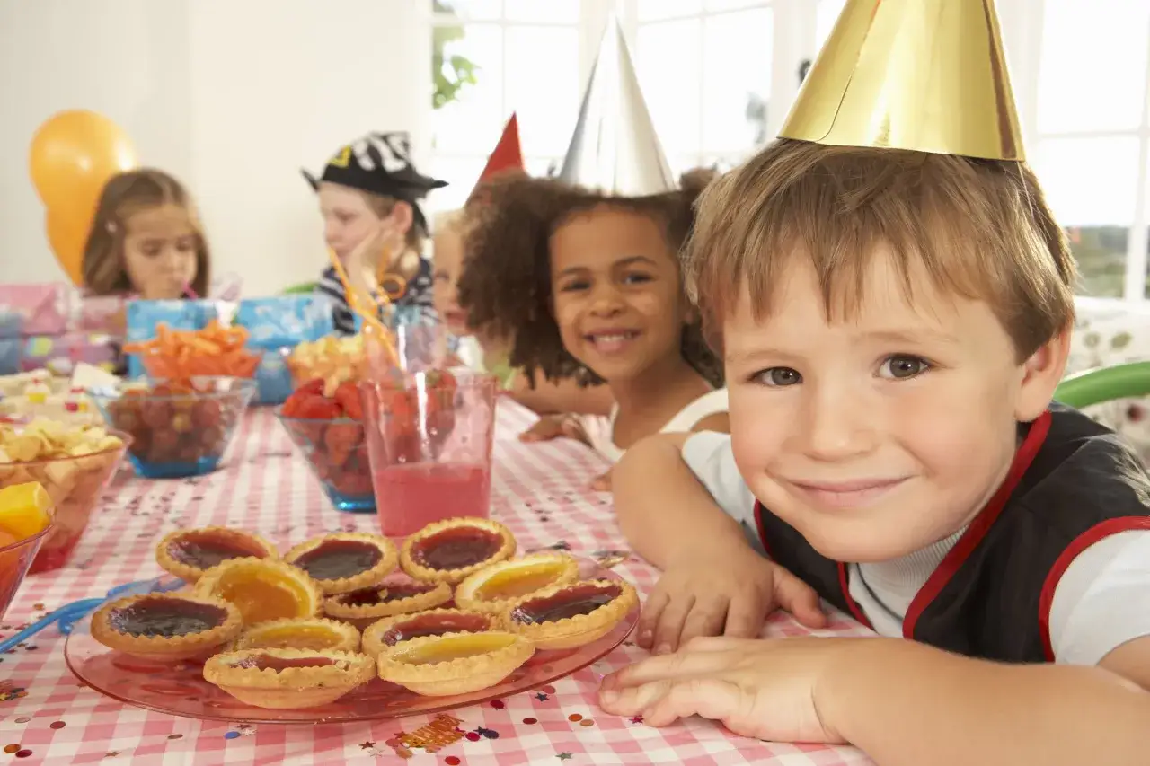 Barn med kalas-hattar njuter av t&aring;rtor och frukt p&aring; ett kalas f&ouml;r 5-&aring;ring.