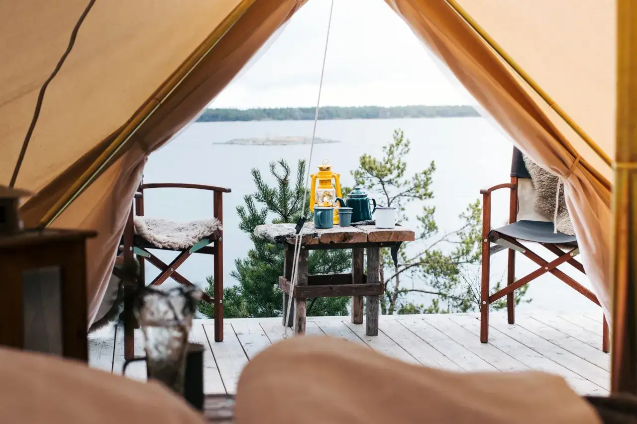 Mysig glamping i Sverige med utsikt &ouml;ver vattnet. En gul lykta, kaffekanna och muggar st&aring;r p&aring; ett rustikt bord.