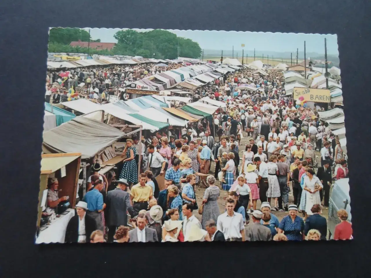 En folkt&auml;t marknad med t&auml;lt och st&aring;nd. En glimt av kiviks marknad historia, med folk i sommarkl&auml;der.