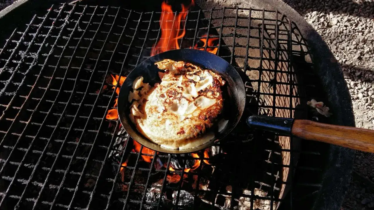 Kolbulle recept tillagas &ouml;ver &ouml;ppen eld. En gyllene pannkaka med fl&auml;sk steks i en gjutj&auml;rnspanna p&aring; ett grillgaller.