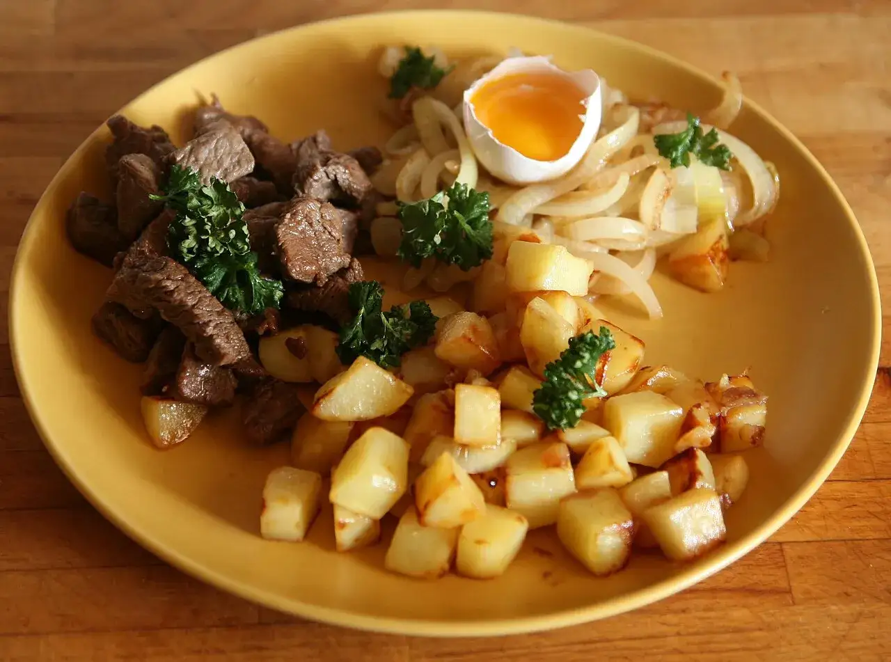 En tallrik med stekt k&ouml;tt, potatis, l&ouml;k och ett &auml;gg. Ett utm&auml;rkt mat tips f&ouml;r en m&auml;ttande m&aring;ltid.