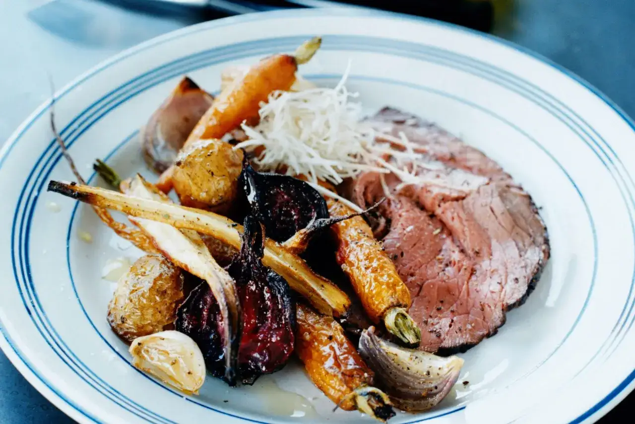 En tallrik med skivad rostbiff, rostade rotfrukter som morötter och palsternacka, samt vitlök. Ett perfekt rostbiff recept för en härlig middag.