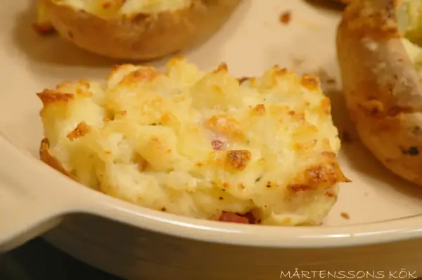 En närbild på en krämig, osttäckt bakad potatis fylld med baconbitar.