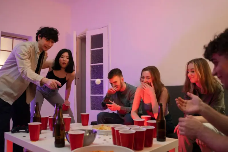Unga vänner spelar beer pong, en rolig aktivitet med röda muggar och skratt.
